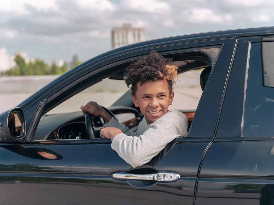 Leerling kijkt lachend uit het raam van de lesauto na zijn proefles
